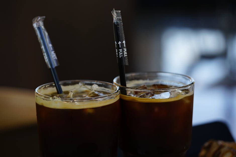Close-up of iced coffee in two glasses with straws on a dark background.